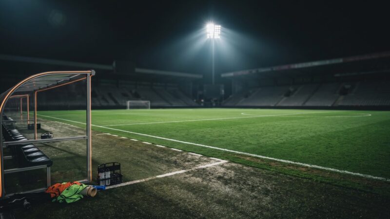 Een verlicht voetbalveld gezien vanaf de zijlijn bij de dug-out, sfeerbeeld bij de trainers van FC Twente