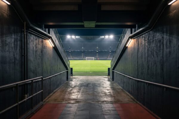 Een spelerstunnel met uitzicht op een verlicht voetbalveld, sfeerbeeld bij de trainers van FC Utrecht