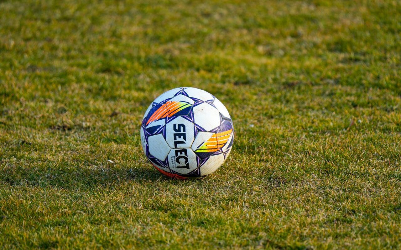 Een witte voetbal ligt in warm zonlicht op een groen grasveld.