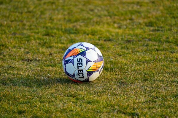 Een witte voetbal ligt in warm zonlicht op een groen grasveld.