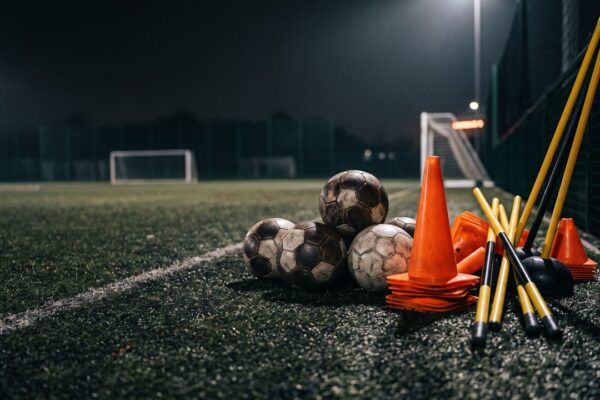 Voetballen, pionnen en slalomstokken langs de lijn van een verlicht trainingsveld, sfeerbeeld bij de trainers van PSV
