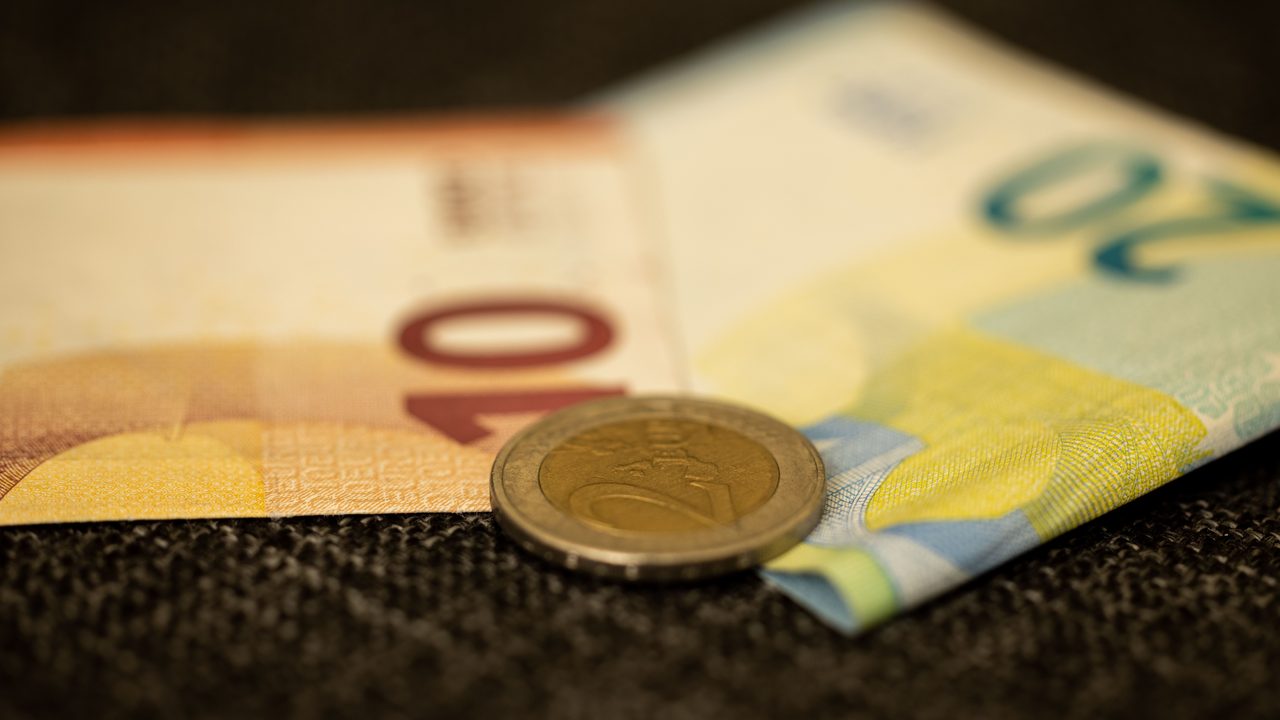 Eurobiljetten en een muntstuk van twee euro op een donkere ondergrond, symbool voor het onbekende fortuin van een assistent-trainer