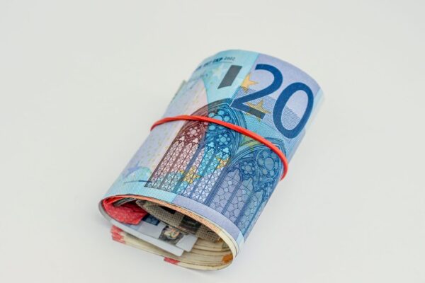 Een opgerolde bundel eurobiljetten met een rood elastiek, symbool voor het fortuin van een wereldreizende trainer