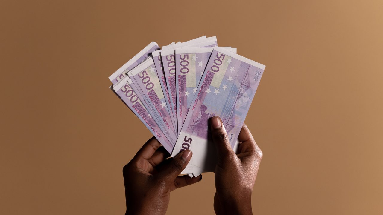 Handen met 500-eurobiljetten op een neutrale achtergrond, symbool voor de verdiensten van een tv-persoonlijkheid