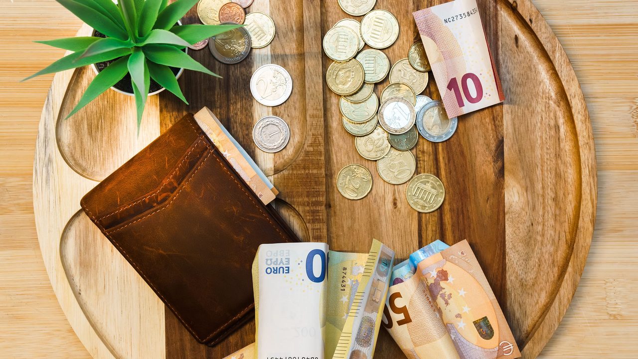 Eurobiljetten en munten op een houten dienblad, symbool voor de verdiensten van een oud-topspits